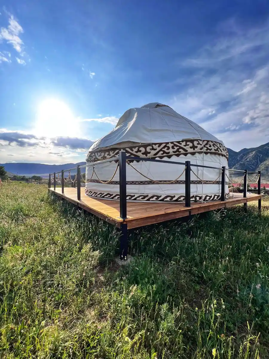 White tourist yurt on a wooden platform in Kolsai with bright sun and mountains behind